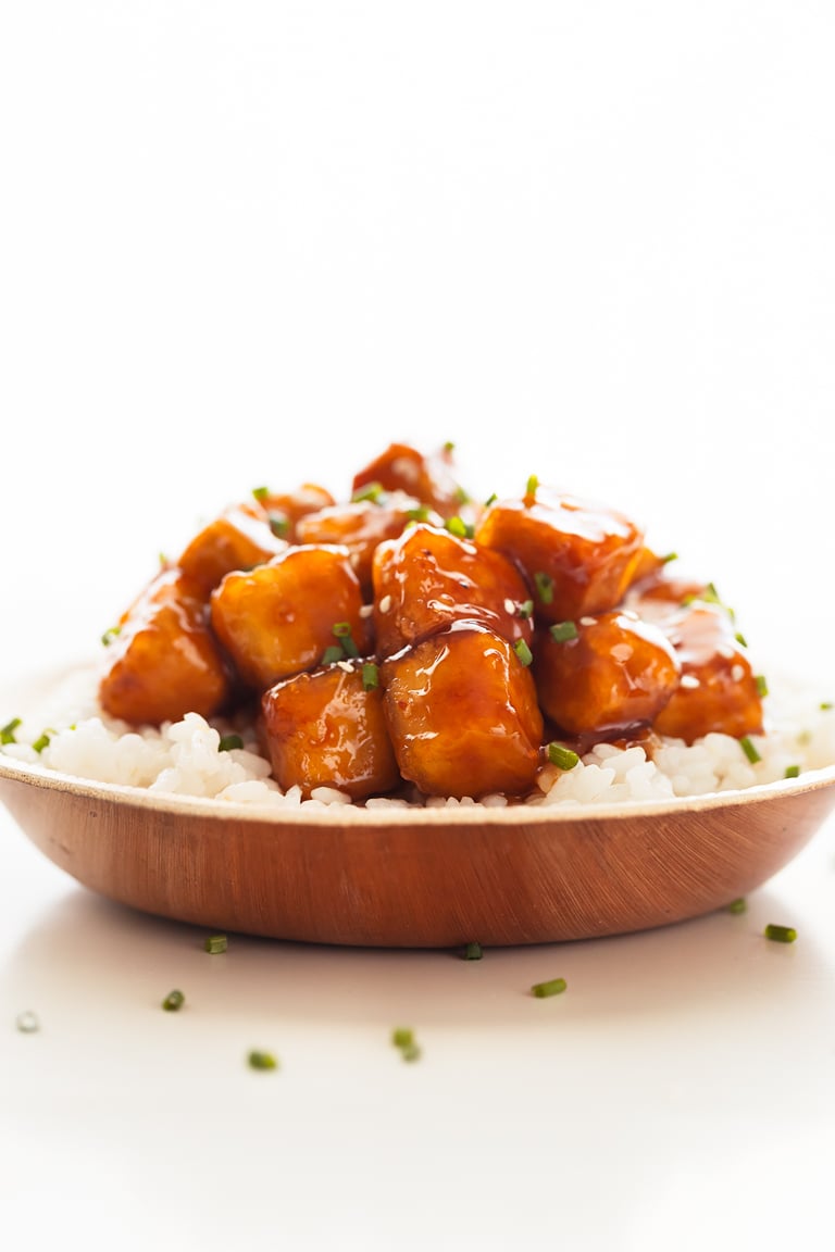 A side shot of a dish with General Tso's tofu served onto cooked white rice