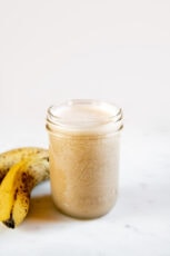 A picture of a jar with banana milk and a couple of bananas
