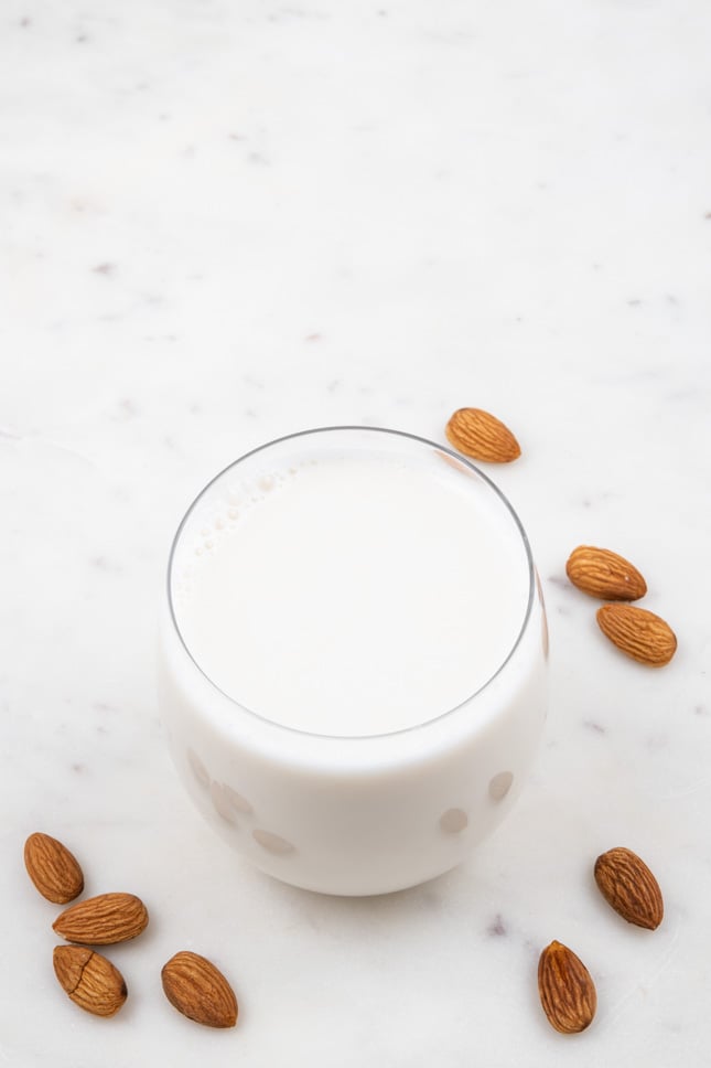 Photo of a glass of almond milk sorrounded by some almonds